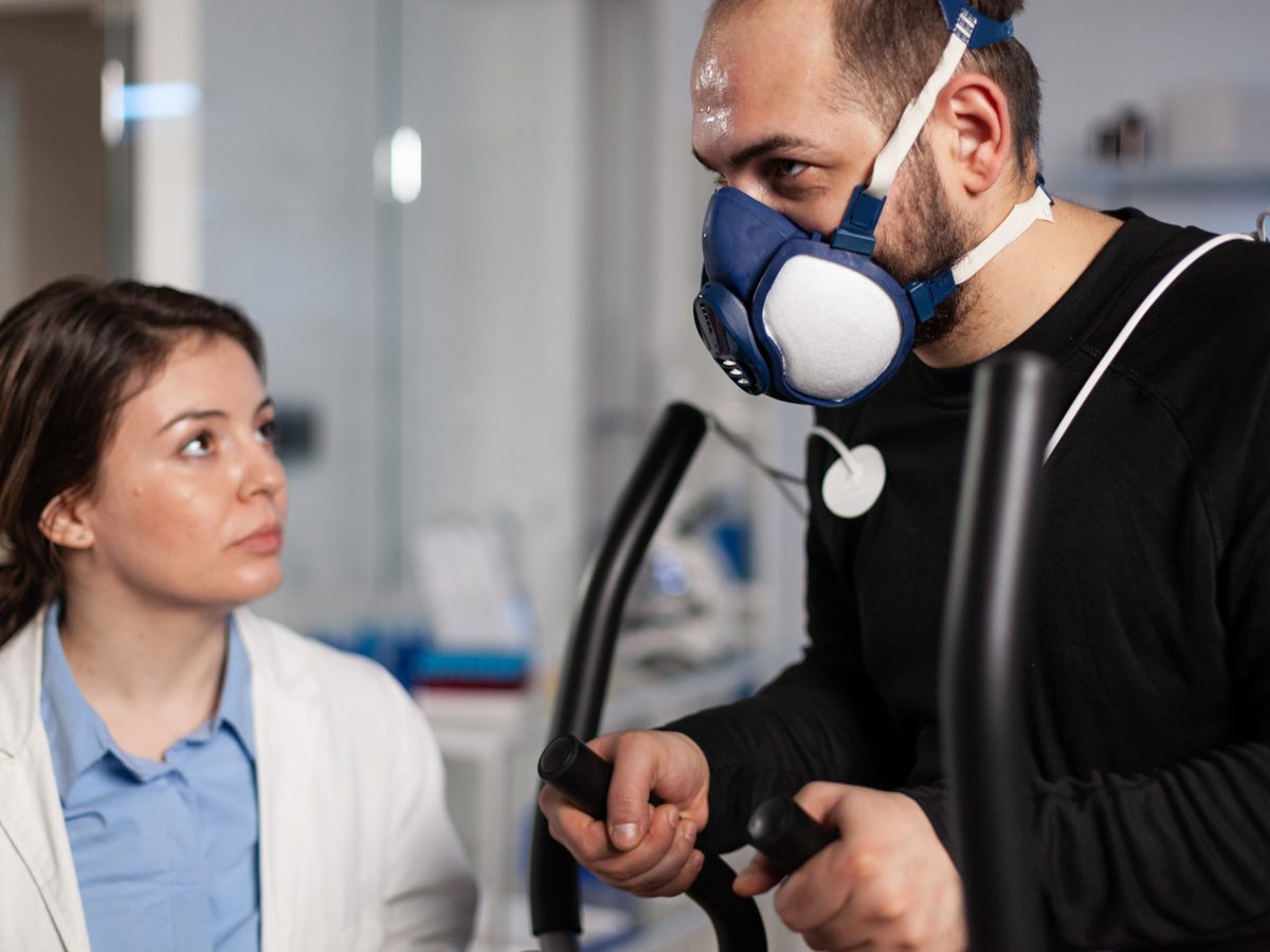 Paciente realizando exame de calorimetria com máscara respiratória acompanhado por profissional