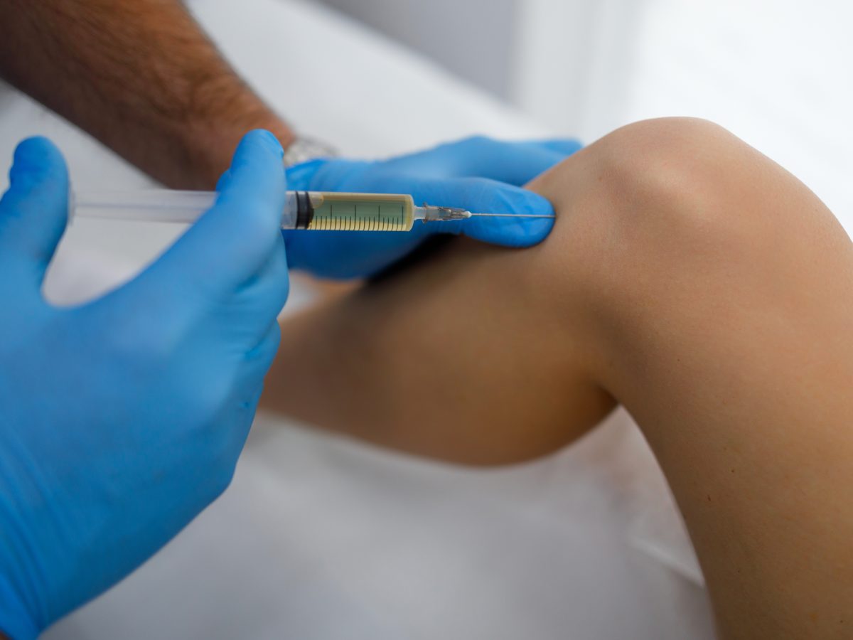 Médico realizando infiltração no joelho de paciente